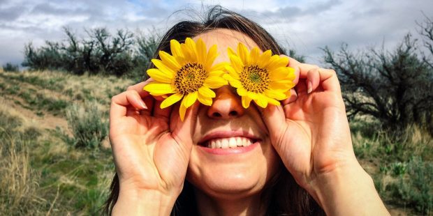 Caucasian woman holding flowers over her eyes  20-24 years, arms raised, brunette, caucasian, close up, color image, covering, day, energy, enthusiasm, eye, flower, front view, happy, head and shoulders, holding, horizontal, mule deer sunflower, nature, obscured face, one person, outdoors, people, photography, playful, playing, portrait, posing, silly, smiling, sunflower, sunny, vitality, woman, young adult, young women, 20-25, 20-30, 20's, 20s, 25-30, absurd, adult, arm, blooming, blossom, blossoming, brown hair, cheerful, close-up, closeup, color, colour, daylight, daytime, eagerness, enclosing, enjoyment, eyeball, female, flora, floral, foolish, gaiety, gal, glad, gleeful, goofy, gusto, head & shoulders, human, human being, jolly, lady, lighthearted, lively, merry, mischievious, mischievous, natural, one, outdoor, outside, person, plant, portraiture, power, raised, raising, ridiculous, satisfaction, smile, spirited, sunlight, sunshine, twenties, twenty, vegetation, wacky, western european, whimsical, women, zeal, zest