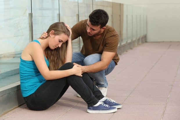 Beautiful teenager girl worried sitting on the floor and a boy comforting her